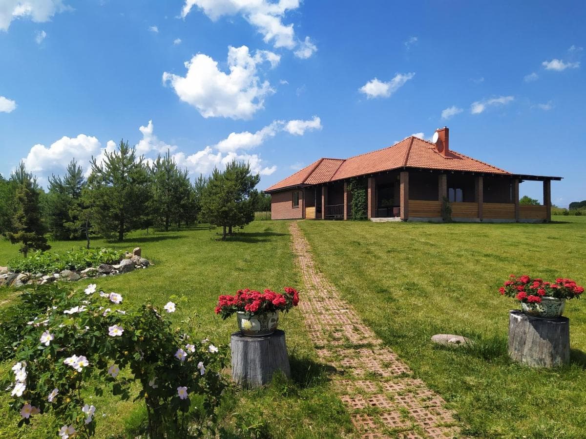 Svečių namas su čerpių stogu, gėlių vazonais ir žydintis pieva